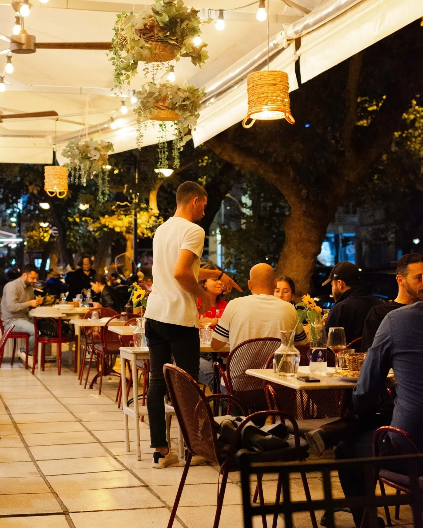 Η βεράντα της Κορωνίς το βράδυ, με φωτισμένα τραπέζια
